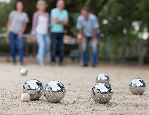 Gros plan sur des boules de pétanques avec les personnes qui lancent derrière.